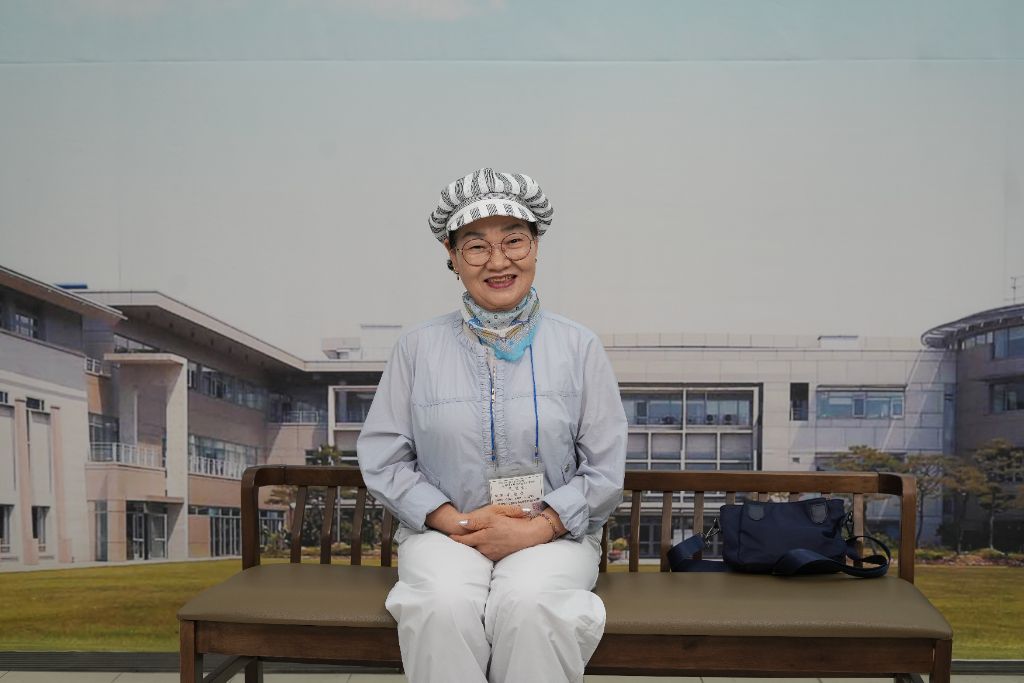 모자를 쓰고 평상복 차림으로 벤치에 앉아 웃고 있는 어르신의 현장 촬영 사진